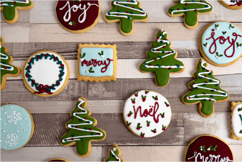 Mit Weihnachtsbäumen und Worten geschmückte Kekse auf einem Holztisch.